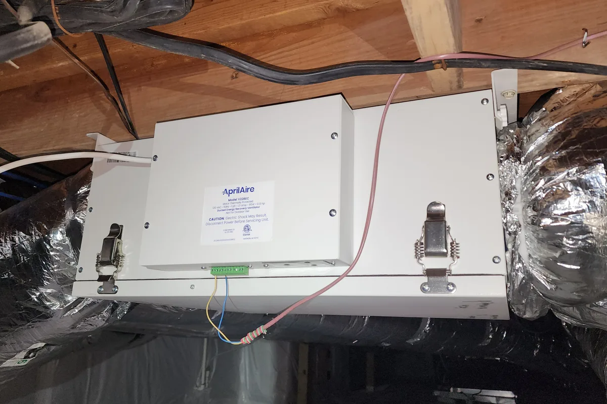 AprilAire V228EC energy recovery ventilator mounted between floor joists in a Wake County NC crawl space, with low-voltage control wiring connected and insulated ductwork alongside