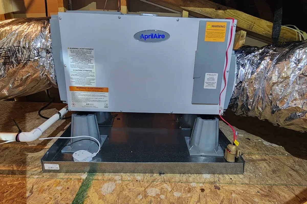 AprilAire whole-house dehumidifier installed on a platform in a Wake County NC attic, connected to insulated supply ductwork