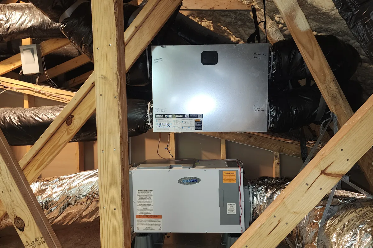 Broan ERV mounted above an AprilAire whole-house dehumidifier in a Wake County NC attic, with fresh-air and exhaust duct connections labeled