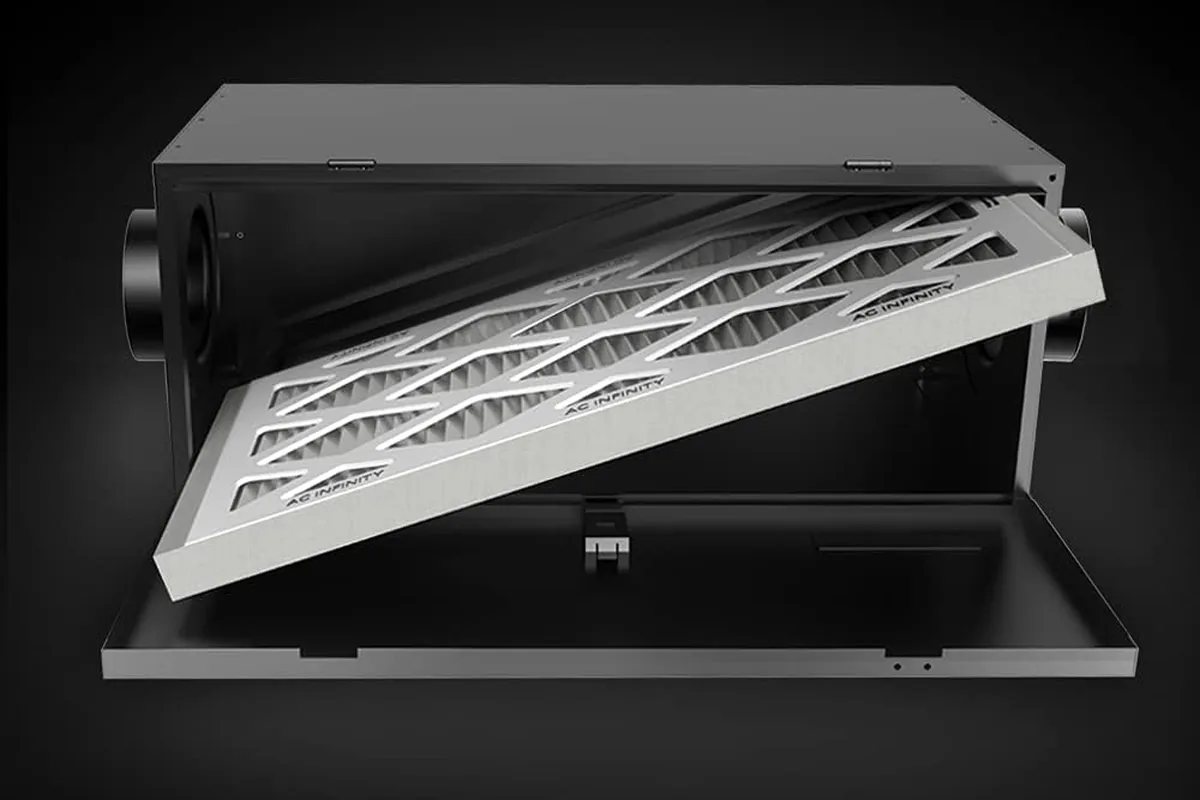 Inline duct filter box with its access door open, showing a pleated MERV media filter sliding into the inner slot, with round duct collars on both ends for connection to the ERV fresh-air intake