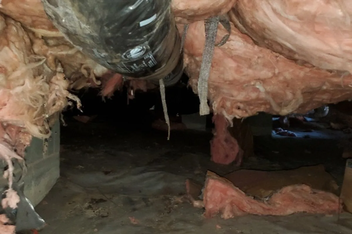 Fiberglass batt insulation sagging from the floor joists, with one batt fallen onto the vapor barrier, in a Triangle NC crawl space
